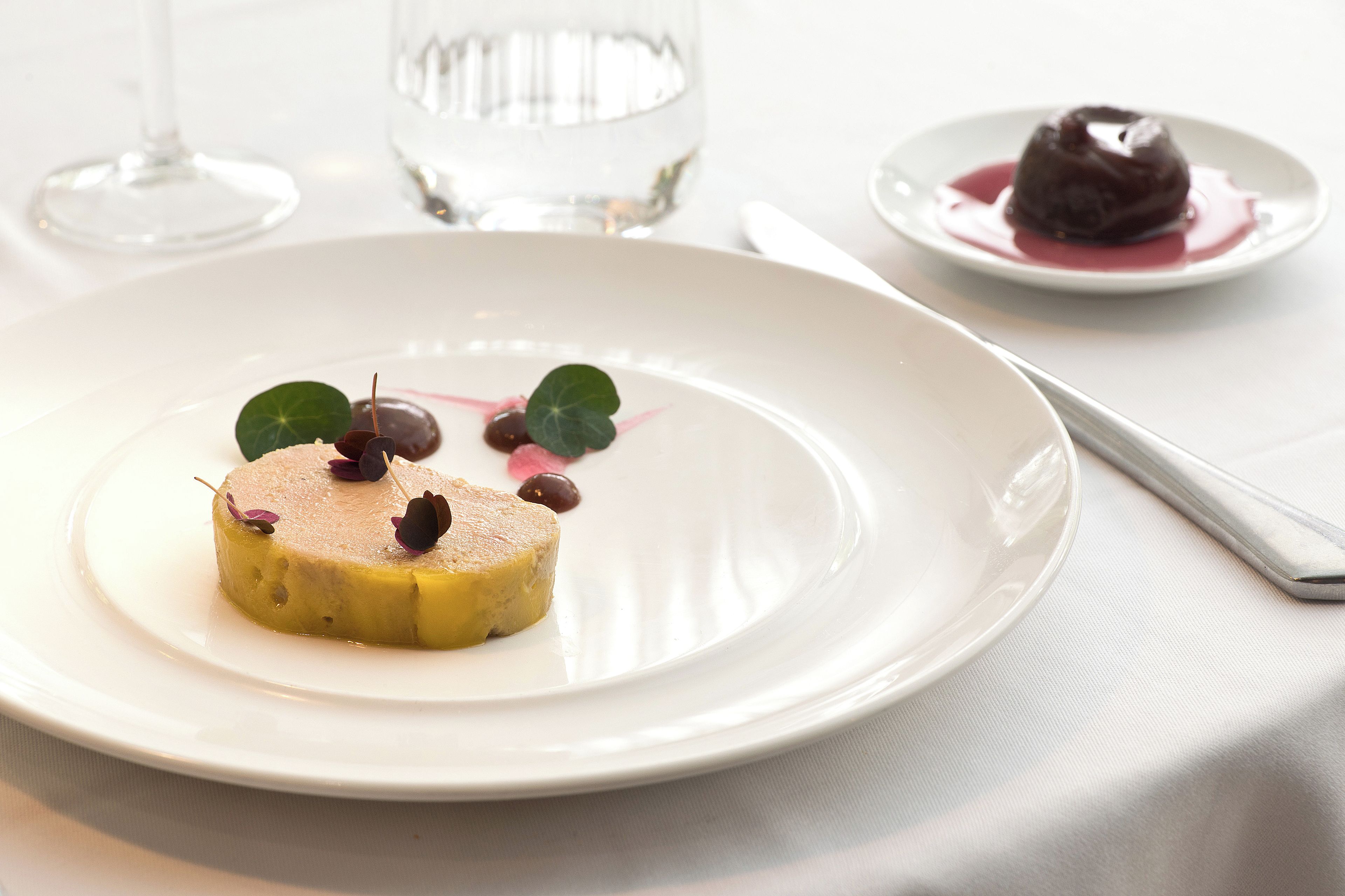 Un dessert servi sur une assiette blanche, avec un verre d’eau et un verre à vin en arrière-plan.