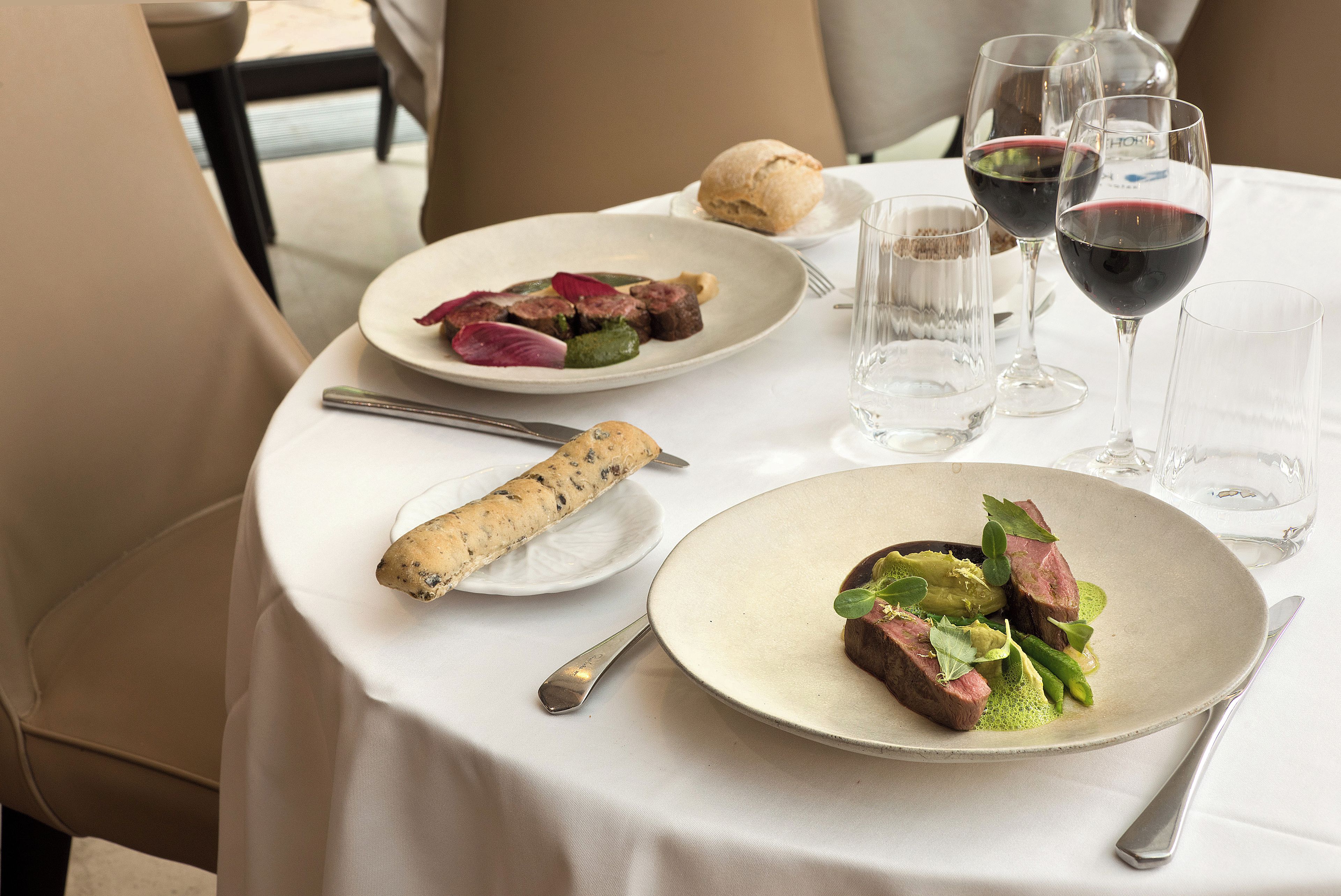 A dining table with plates of food, wine glasses, and cutlery.