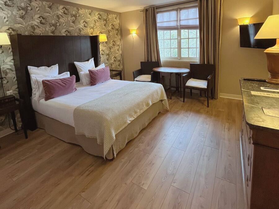Habitación de hotel con una cama grande, una mesita pequeña, dos sillas, un escritorio y un televisor.