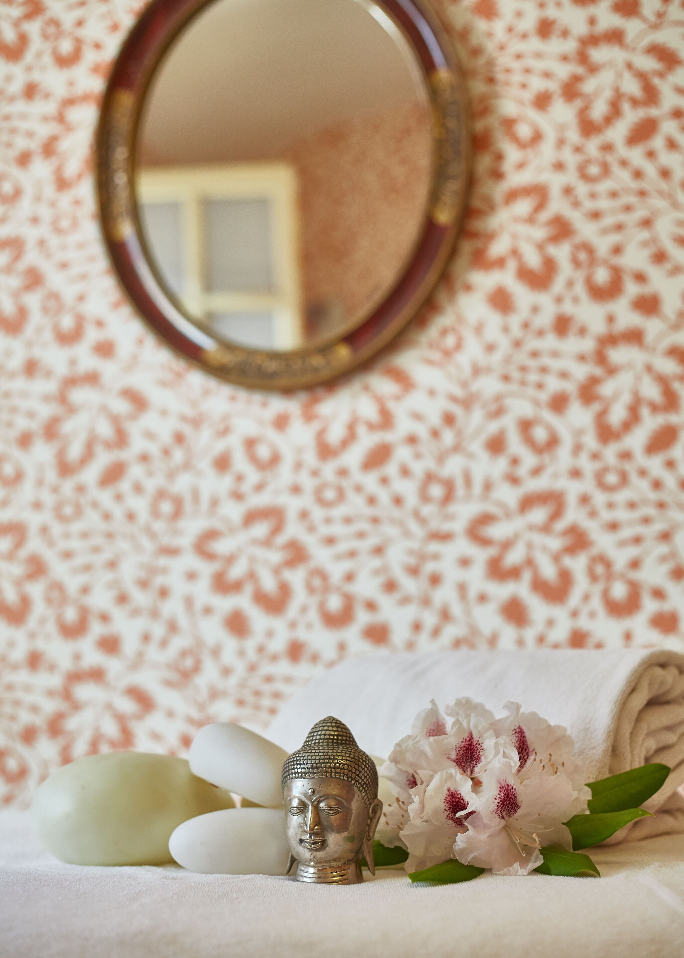 A Buddha statue, a mirror, and a floral arrangement on a white surface.