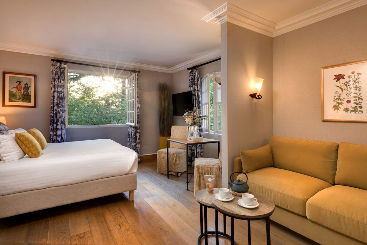 A room with a bed, a sofa, a small table with cups and a teapot, and a window with curtains.