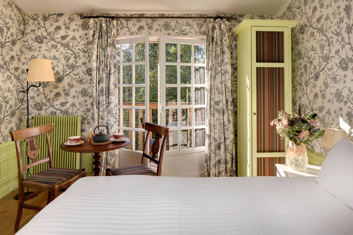 A room with a bed, a table with chairs, a window with curtains, and a door with a striped panel.
