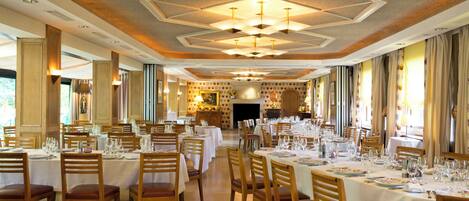 A large dining hall with multiple tables set for a meal, wooden chairs, and a decorative ceiling.