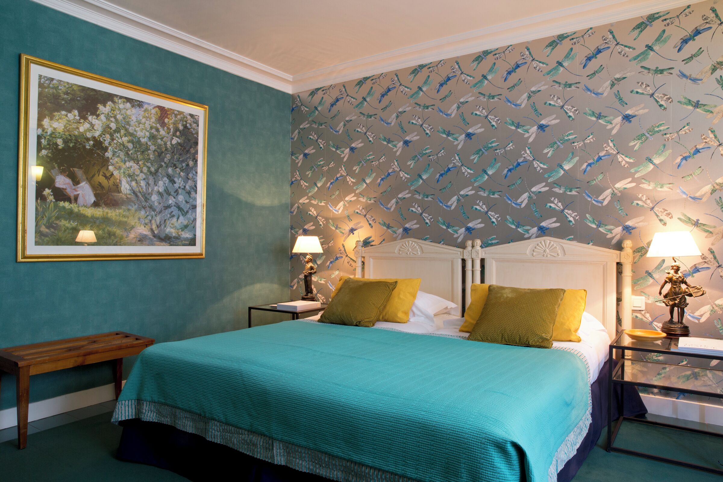 A bedroom with a bed, two nightstands, a bench, a framed picture, and a wall with a bird pattern.