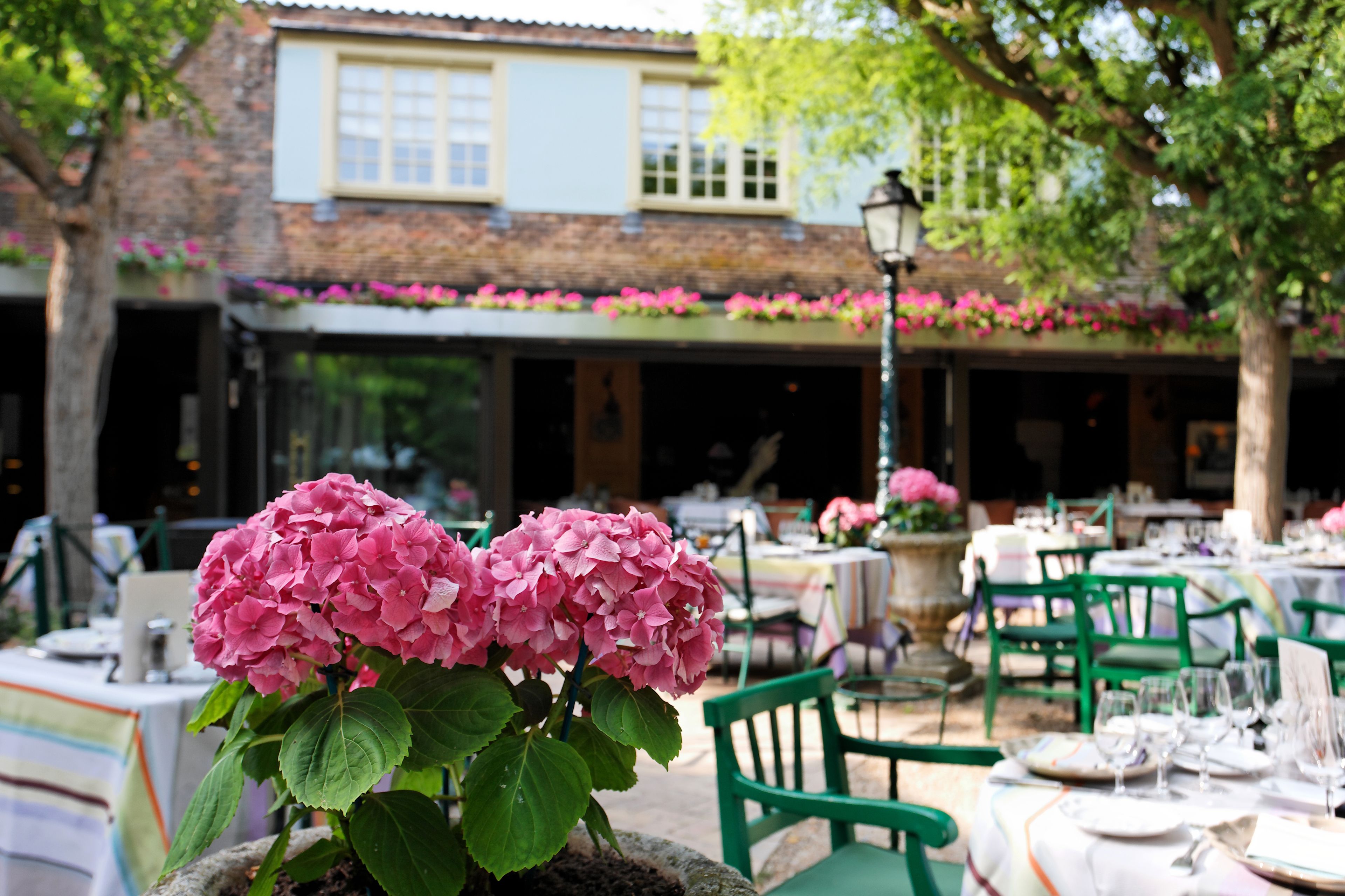 Un ristorante con posti a sedere all'aperto, un'esposizione floreale e un edificio con tetto in tegole sullo sfondo.