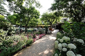 A garden pathway with tables and chairs, surrounded by lush greenery and flowering plants.