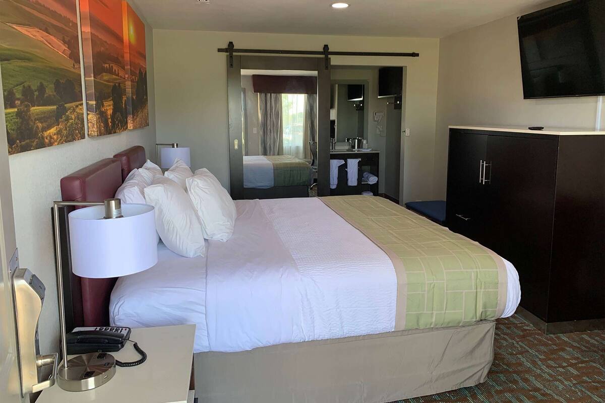 A hotel room with a large bed, a desk with a lamp, a telephone, a television, and a wardrobe.