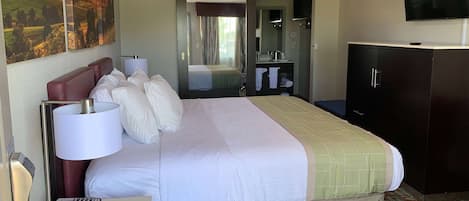 A hotel room with a large bed, a desk with a lamp, a telephone, a television, and a wardrobe.