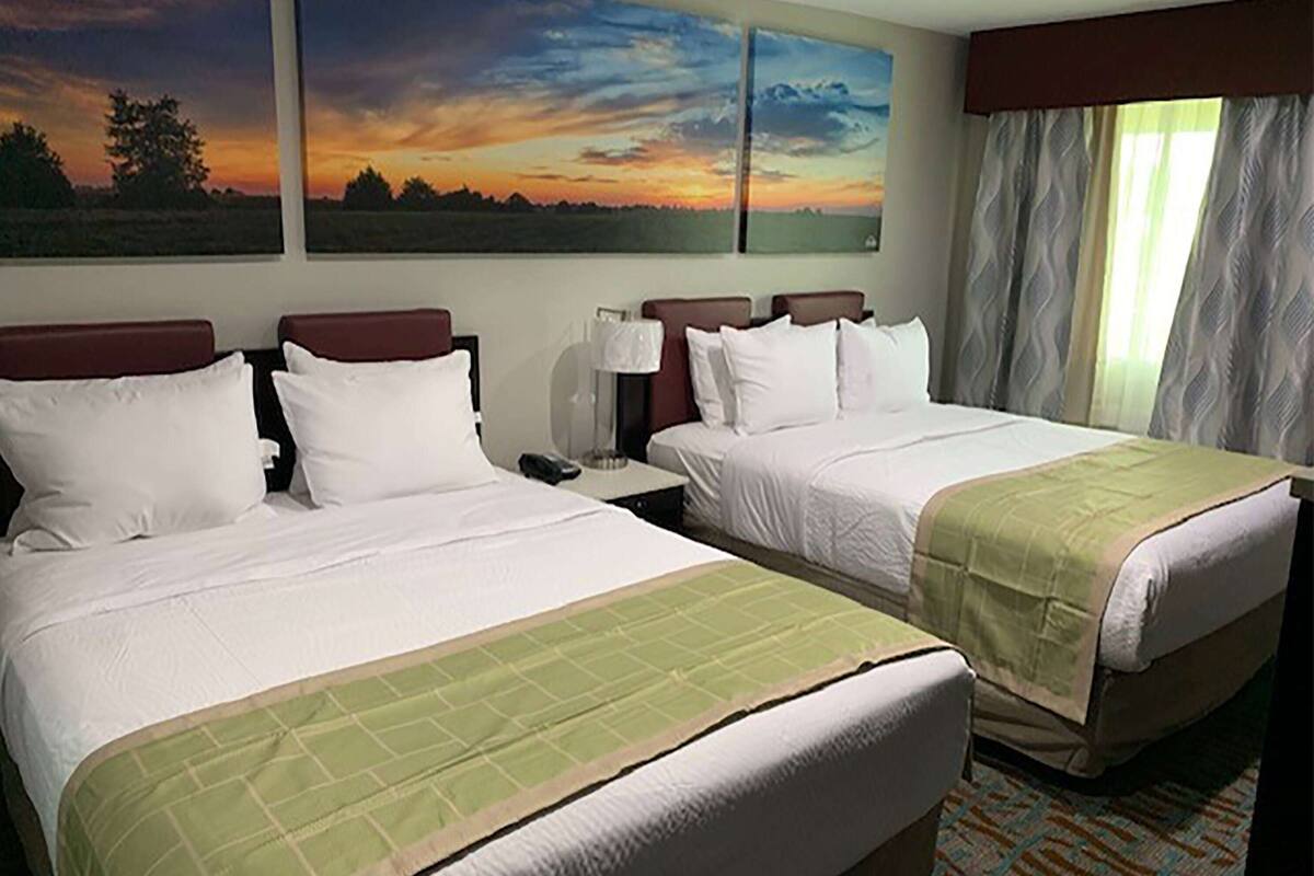 A hotel room with two beds, a nightstand, and a window with curtains.