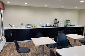 Cozinha moderna com bancada, armários pretos e área de estar com mesas e cadeiras.