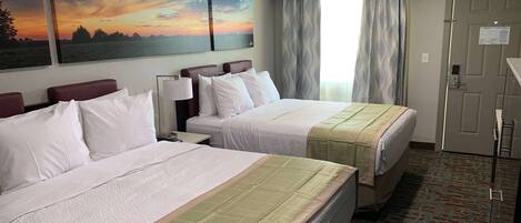 Habitación de hotel con dos camas, un cuadro grande de una puesta de sol, una ventana con cortinas y una puerta con un letrero.