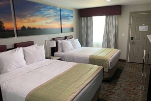A hotel room with two beds, a large painting of a sunset, a window with curtains, and a door with a sign.