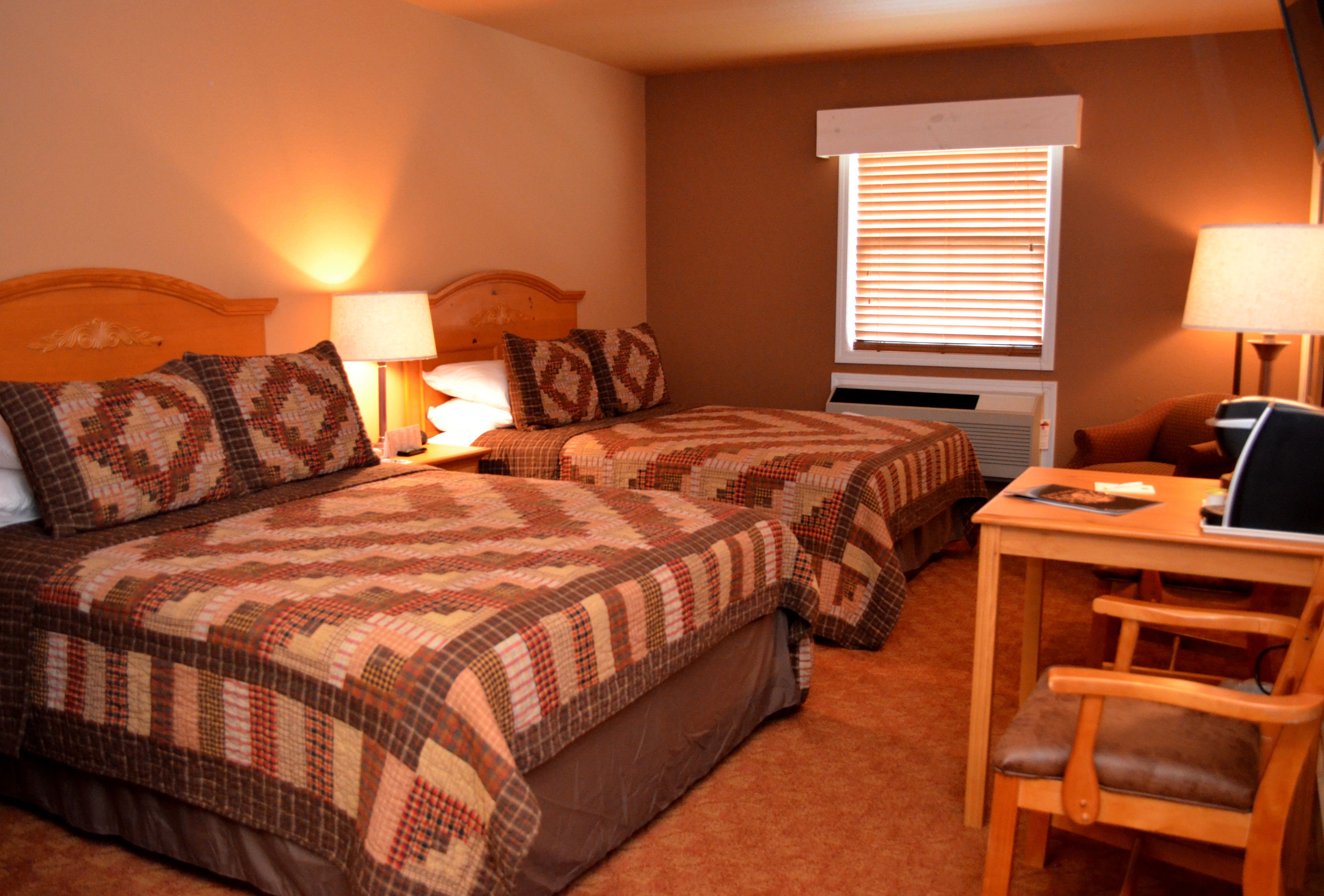 A hotel room with two beds, a desk, a chair, and a window with blinds.