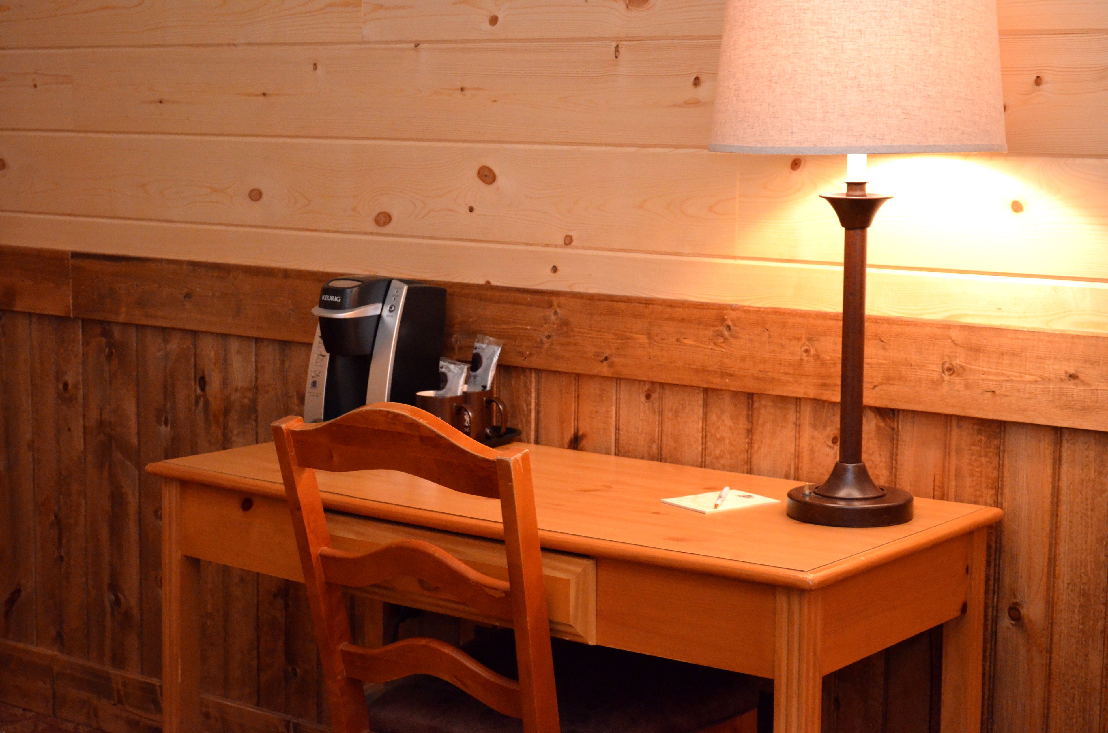 Un bureau en bois, une lampe, une chaise et une petite table sur laquelle se trouvent un livre et une tasse de café.