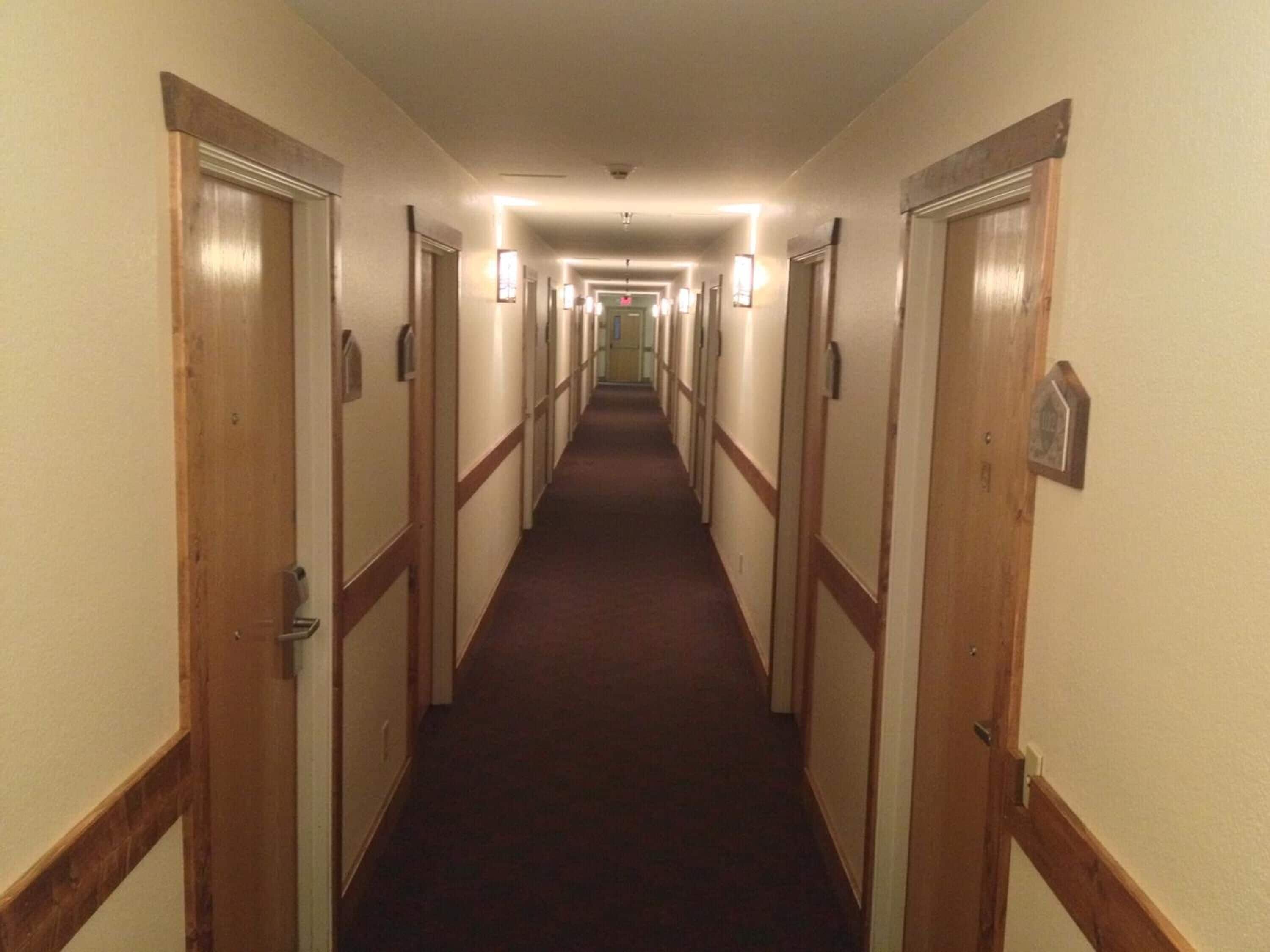 A hotel hallway with wooden doors, carpeted floors, and wall-mounted light fixtures.
