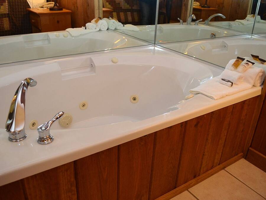 A large, white bathtub with chrome fixtures, a glass-enclosed shower area, and a wooden vanity with a mirror.