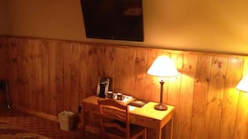 Ein Zimmer mit Holzvertäfelung, einem an der Wand montierten Fernseher, einem Schreibtisch mit Lampe und einem Sessel.