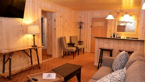 Una habitación acogedora con decoración de madera, un sofá, una mesa de centro, un televisor y un comedor con sillas y una mesa.