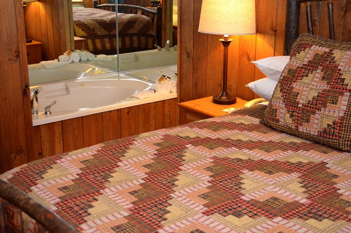 A wooden-paneled room with a bed, a mirror, a lamp, and a bathroom with a bathtub.