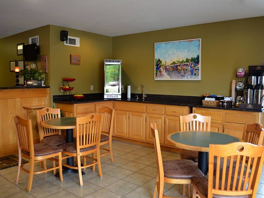 A kitchen with wooden cabinets, a dining table with chairs, a coffee station, and a painting on the wall.