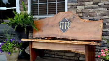 A rustic wooden bench with a shield-shaped plaque bearing the initials "AR" against a stone wall backdrop.