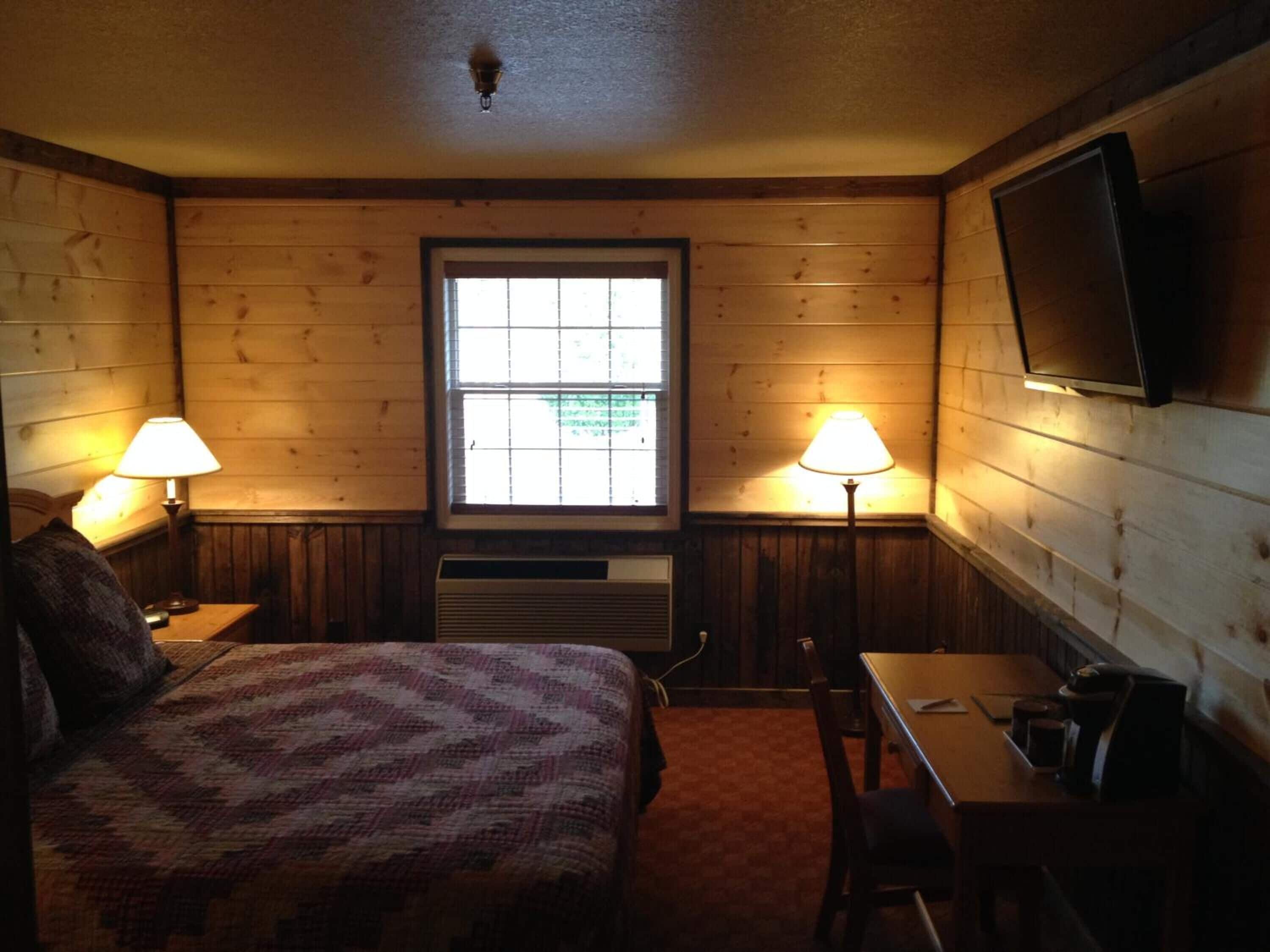 A cozy room with a bed, a desk, a chair, a TV, and two lamps.