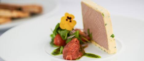 A white plate with a piece of meat, a flower, and some greens.