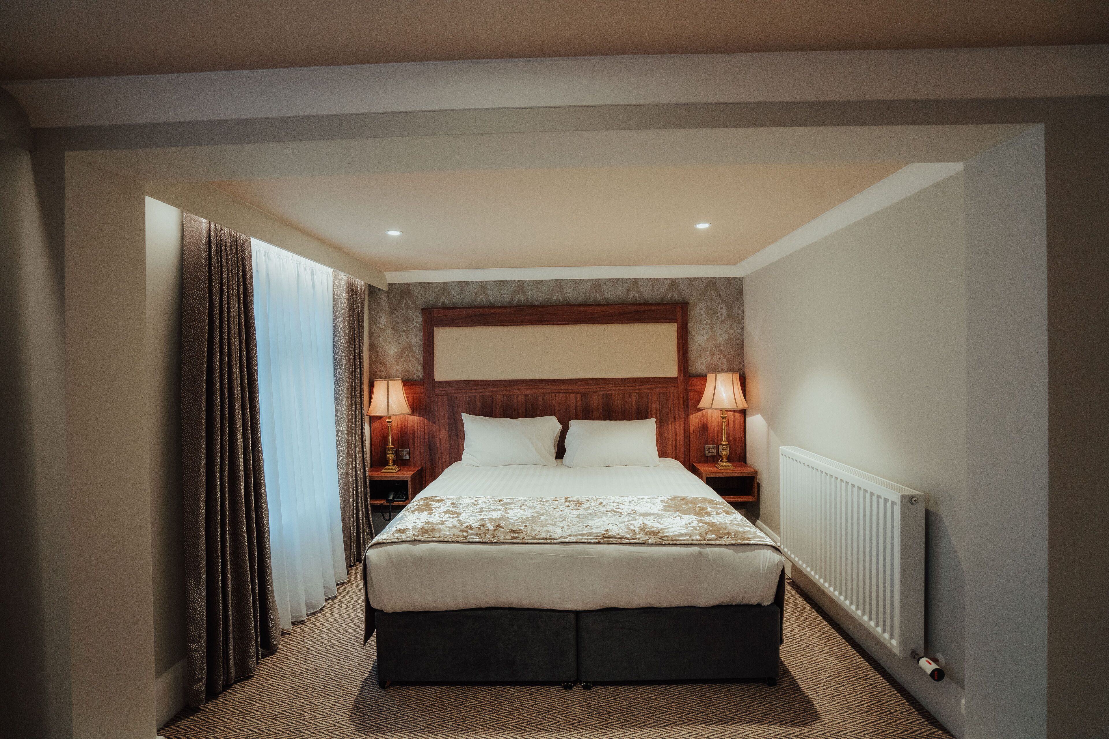 Une chambre d’hôtel avec un grand lit, deux tables de chevet avec des lampes, une tête de lit et un radiateur.
