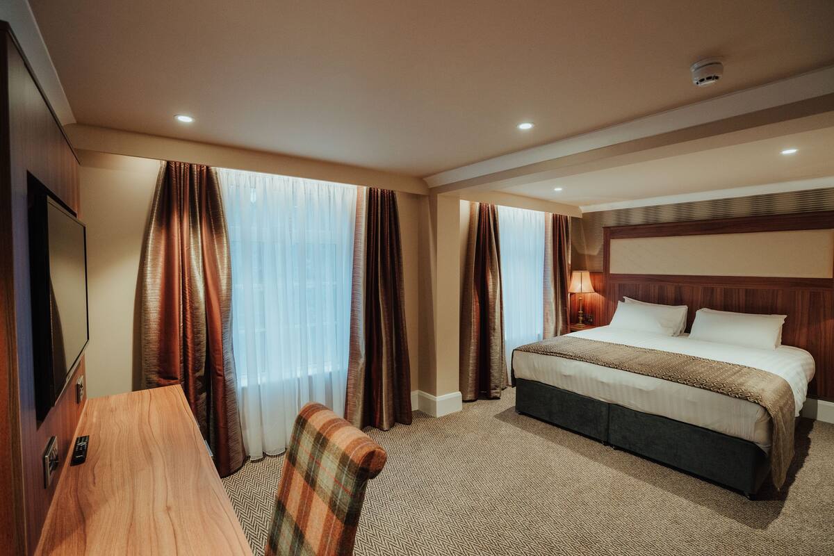 Quarto de hotel com cama, secretária, cadeira e televisão.