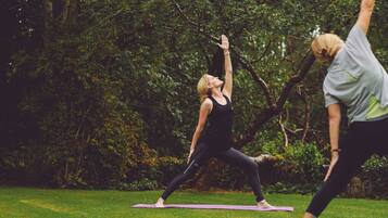 A person performing a yoga pose on a mat in a park with trees in the background.