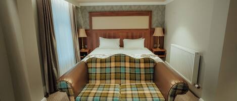 Une chambre d’hôtel avec un grand lit, deux tables de chevet, une tête de lit, une fenêtre avec des rideaux et un canapé.