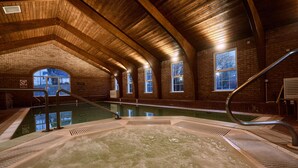 A hot tub in a room with brick walls and wooden beams, large windows, and a pool. - Dunadry Hotel and Gardens (Antrim)