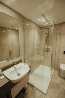 Un baño moderno con ducha envuelta en vidrio, un lavabo blanco y un espejo grande.