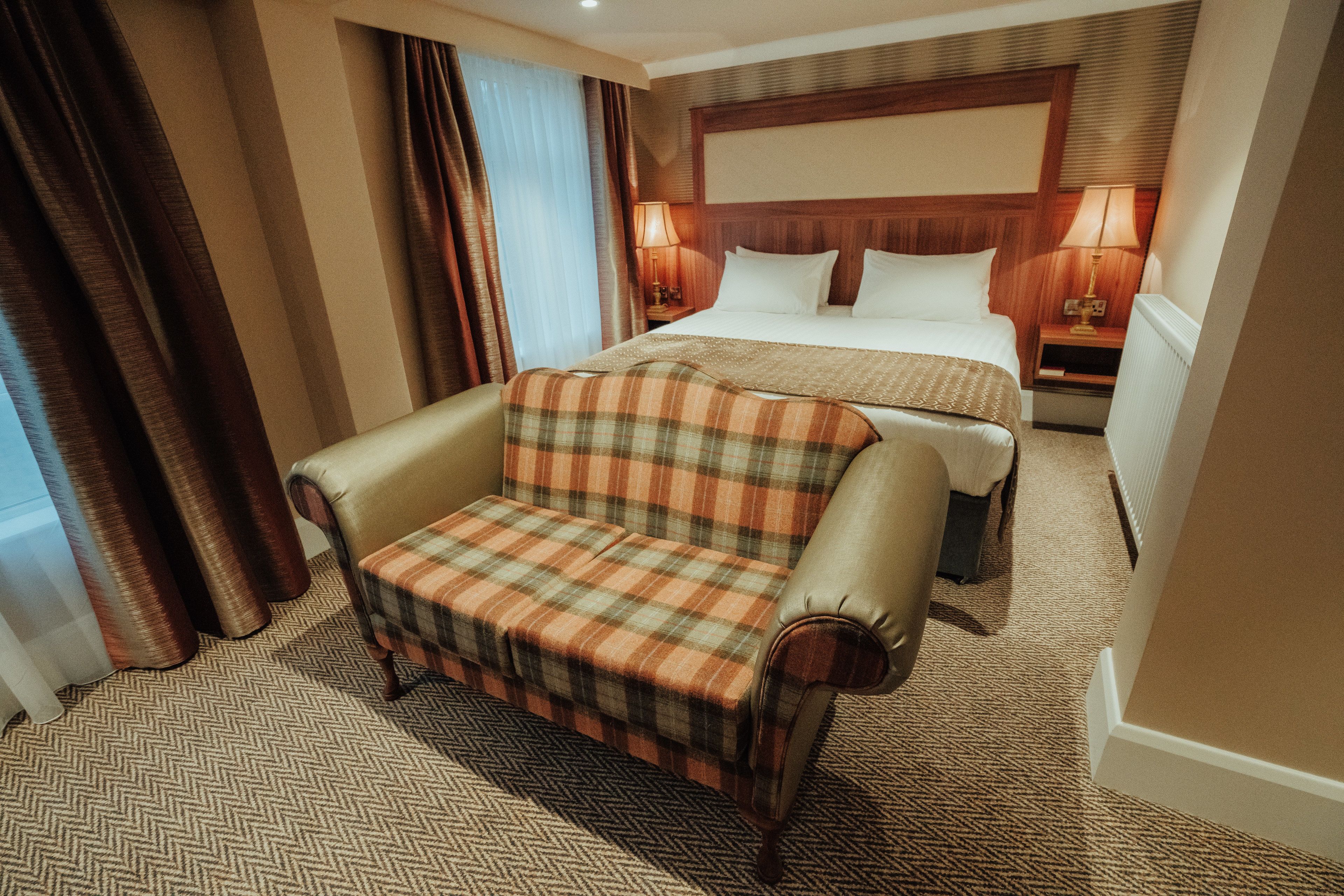 Una habitación de hotel con cama, sofá, mesita de noche y lámpara.
