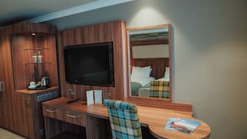 Habitación de hotel compacta con escritorio de madera, televisor, cama con cabecero y espejo.