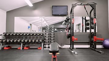 A gym with weightlifting equipment, a TV, and a mirror.