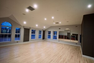 Una habitación amplia con suelo de madera, ventanas grandes y un espejo.