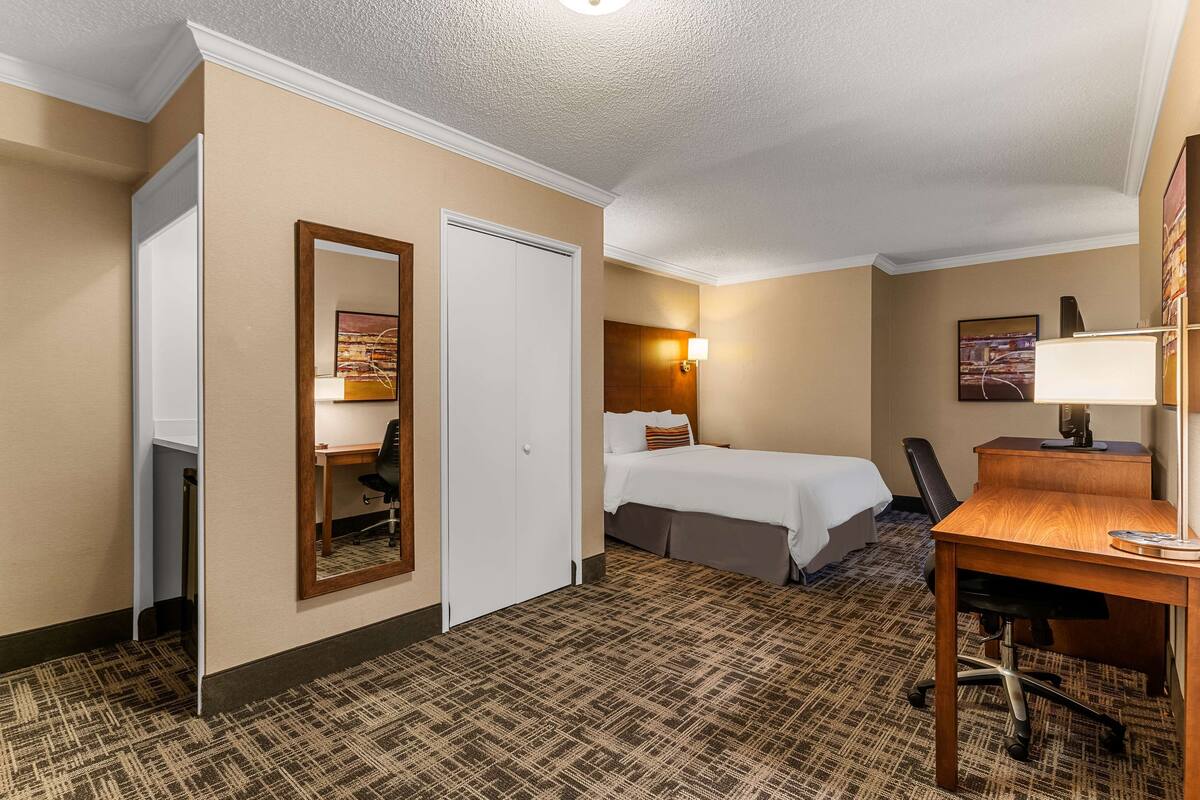 Una habitación de hotel con cama, escritorio, silla y espejo.