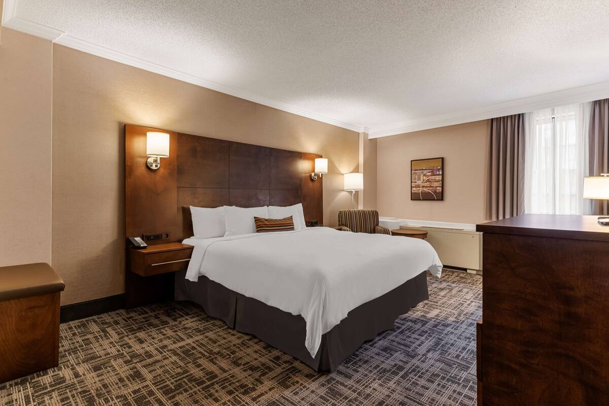 Una habitación de hotel con una cama grande, un cabecero de madera, dos lámparas de noche, una mesita de noche, un escritorio y una silla.