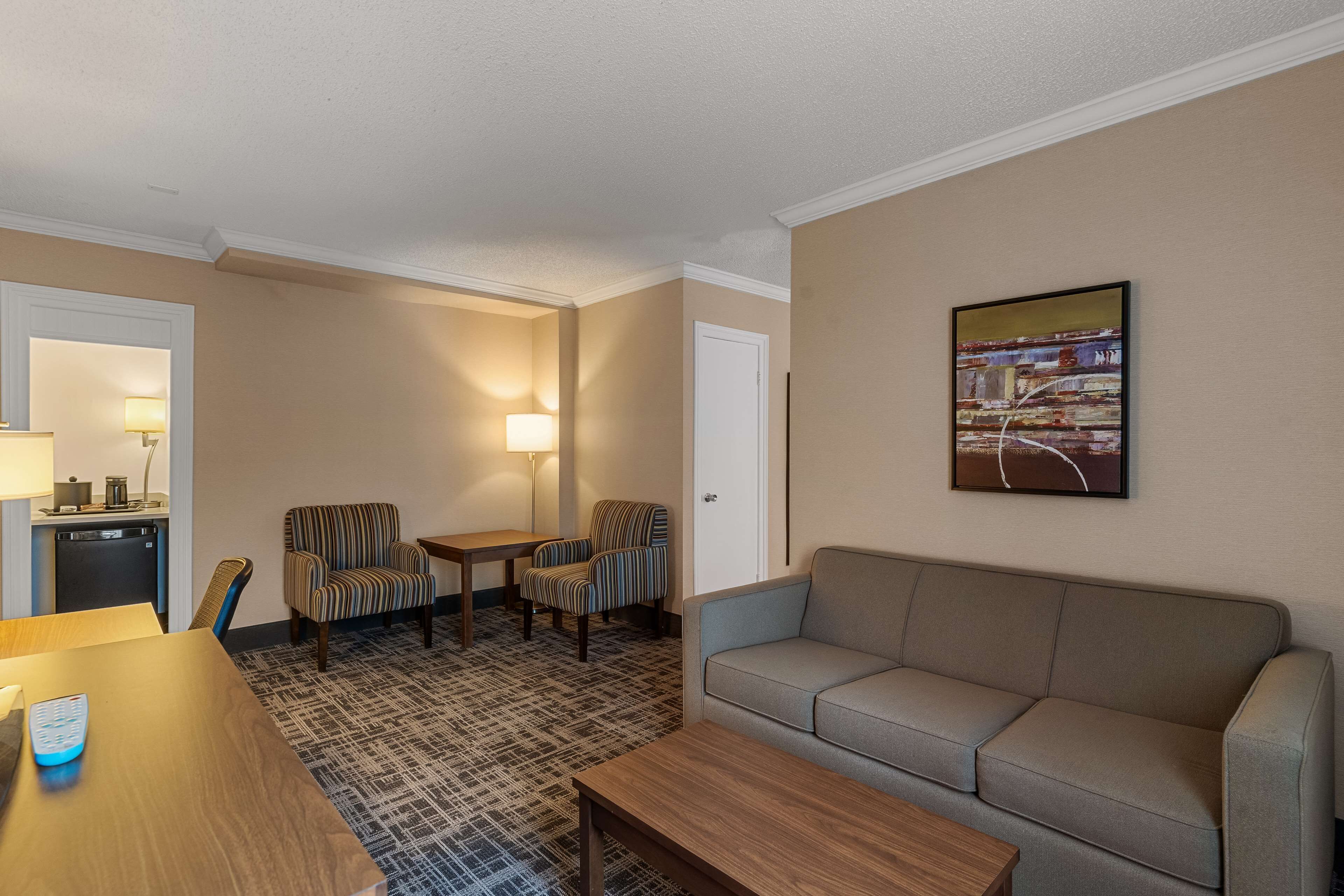 Una habitación de hotel con un sofá, dos sillones, una mesita y una lámpara.
