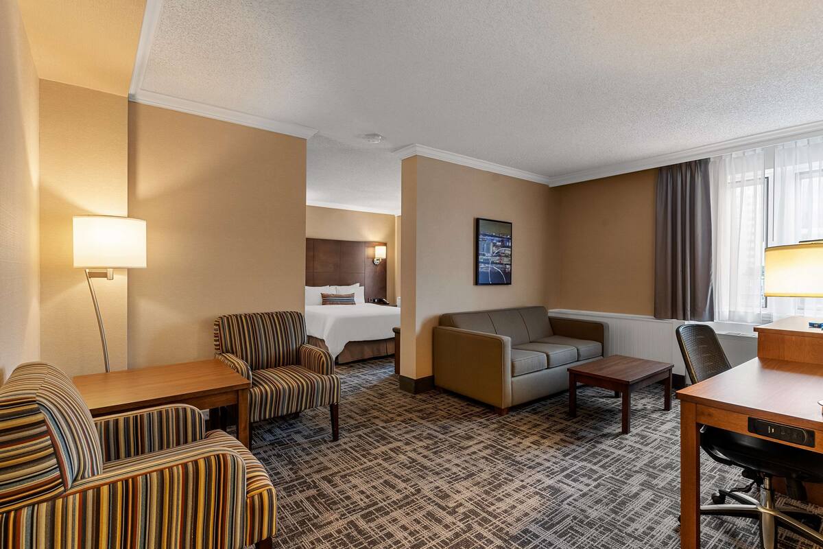 Una habitación de hotel con una cama, un sofá, un sillón a rayas, un escritorio y una lámpara.