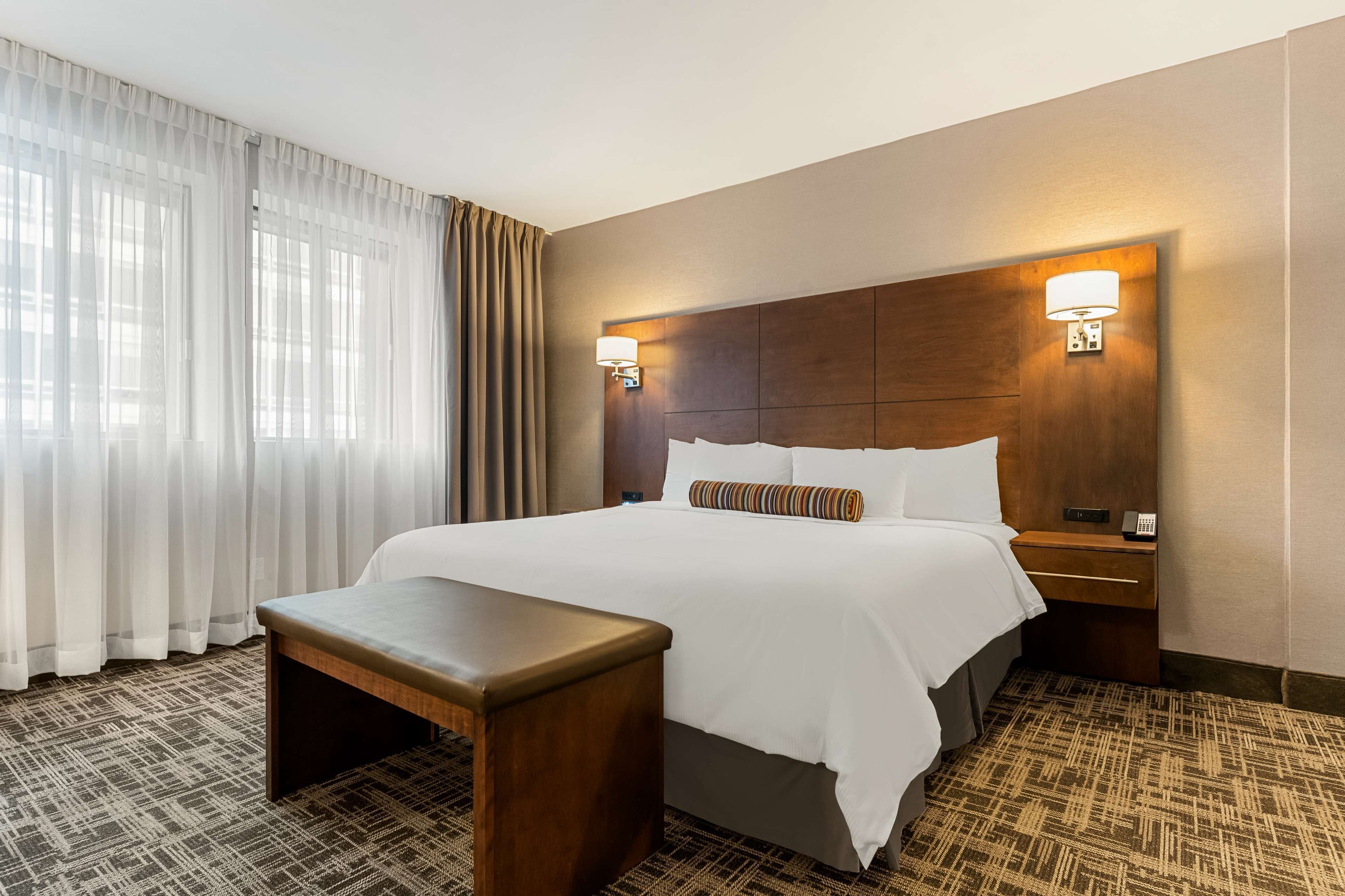 A hotel room with a large bed, a bedside table, a lamp, and a patterned carpet.