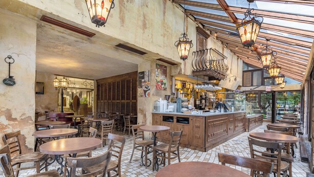 Un café con mesas y sillas redondas, una zona de bar y suelo de baldosas.