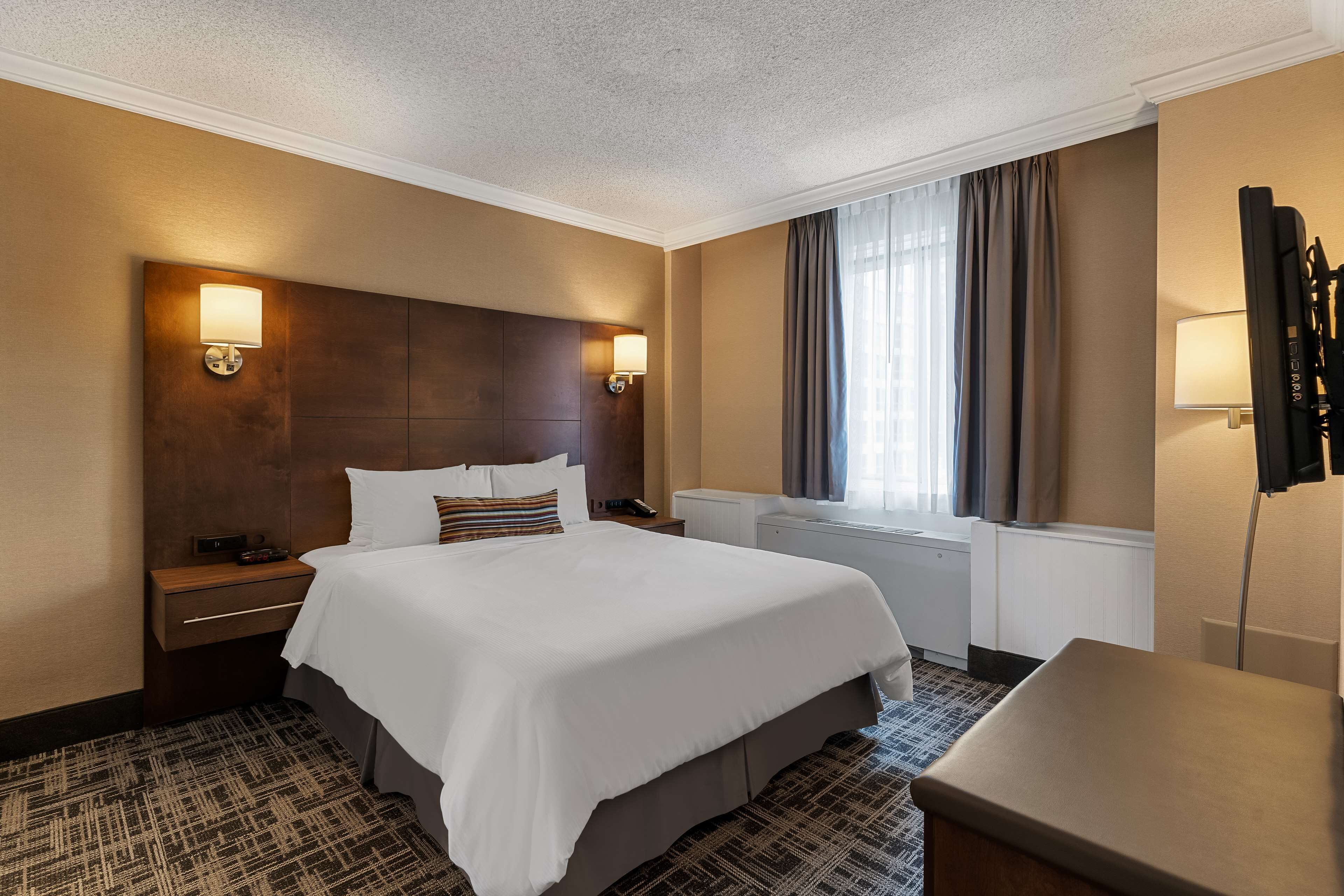 Une chambre d’hôtel avec un grand lit, deux tables de chevet, un bureau, un téléviseur à écran plat et une fenêtre avec des rideaux.