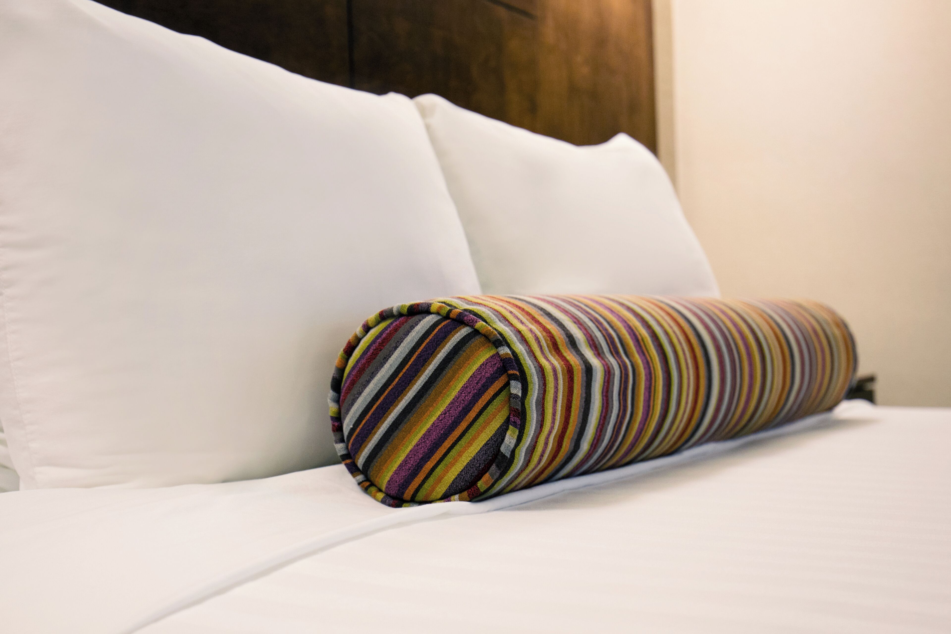 Una cama bien hecha con sábanas blancas y una toalla a rayas enrollada.