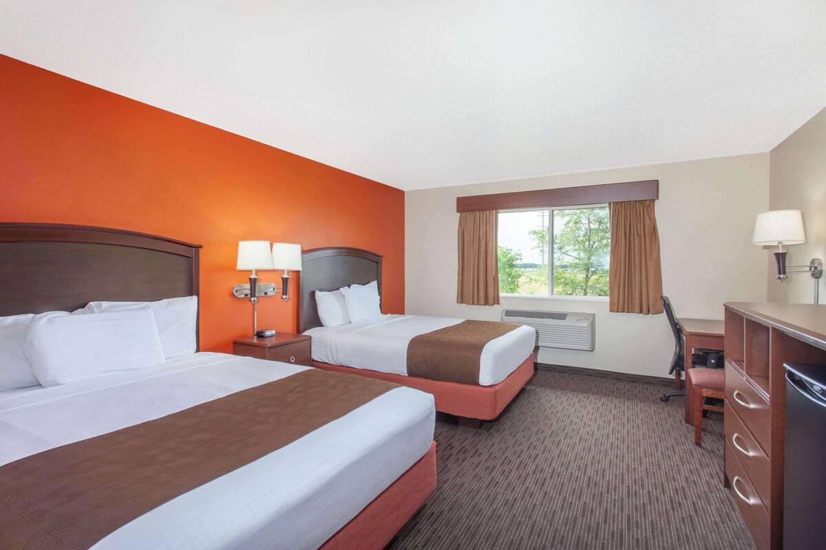 A hotel room with two beds, a desk, a chair, and a dresser.