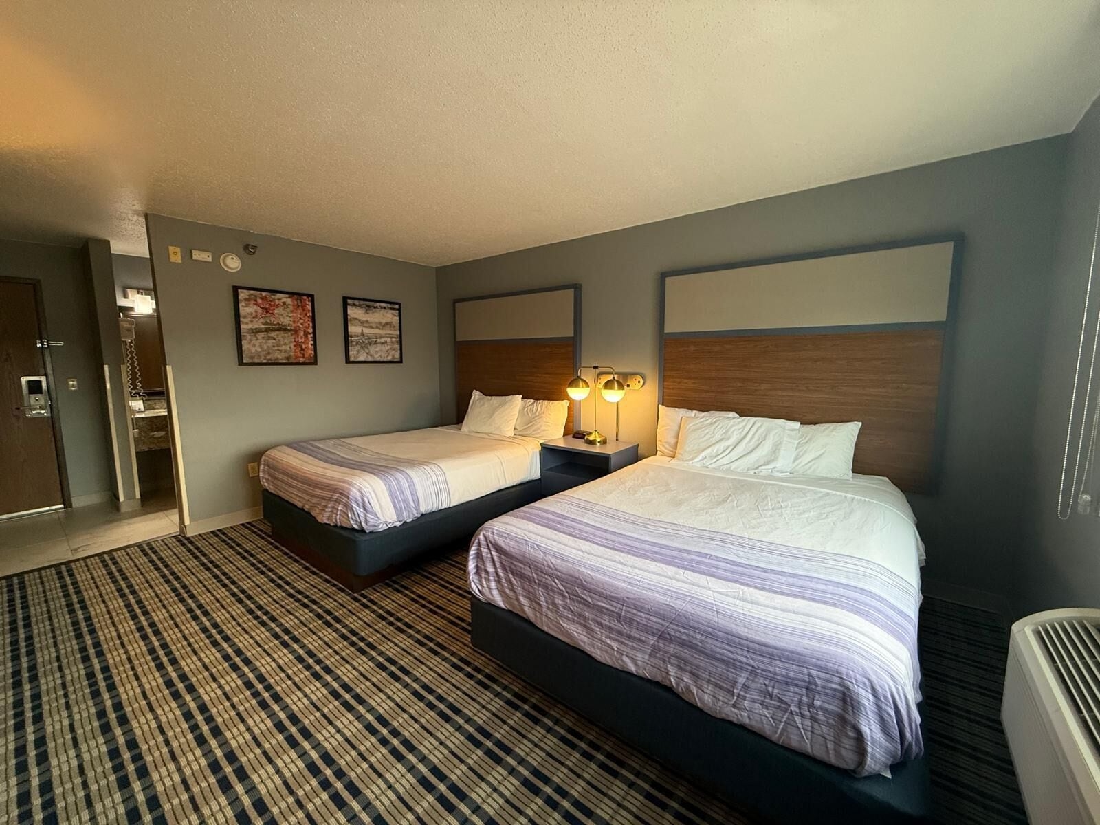 Een hotelkamer met twee bedden, een grote spiegel en een luchtbevoorrachtingsunit aan de muur.