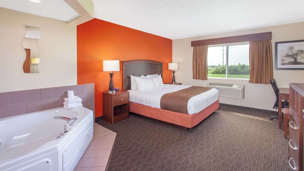 A hotel room with a large bed, a separate bathroom with a bathtub, a desk, and a window with curtains. - AmericInn by Wyndham St. Cloud MN I-94 (St Cloud)