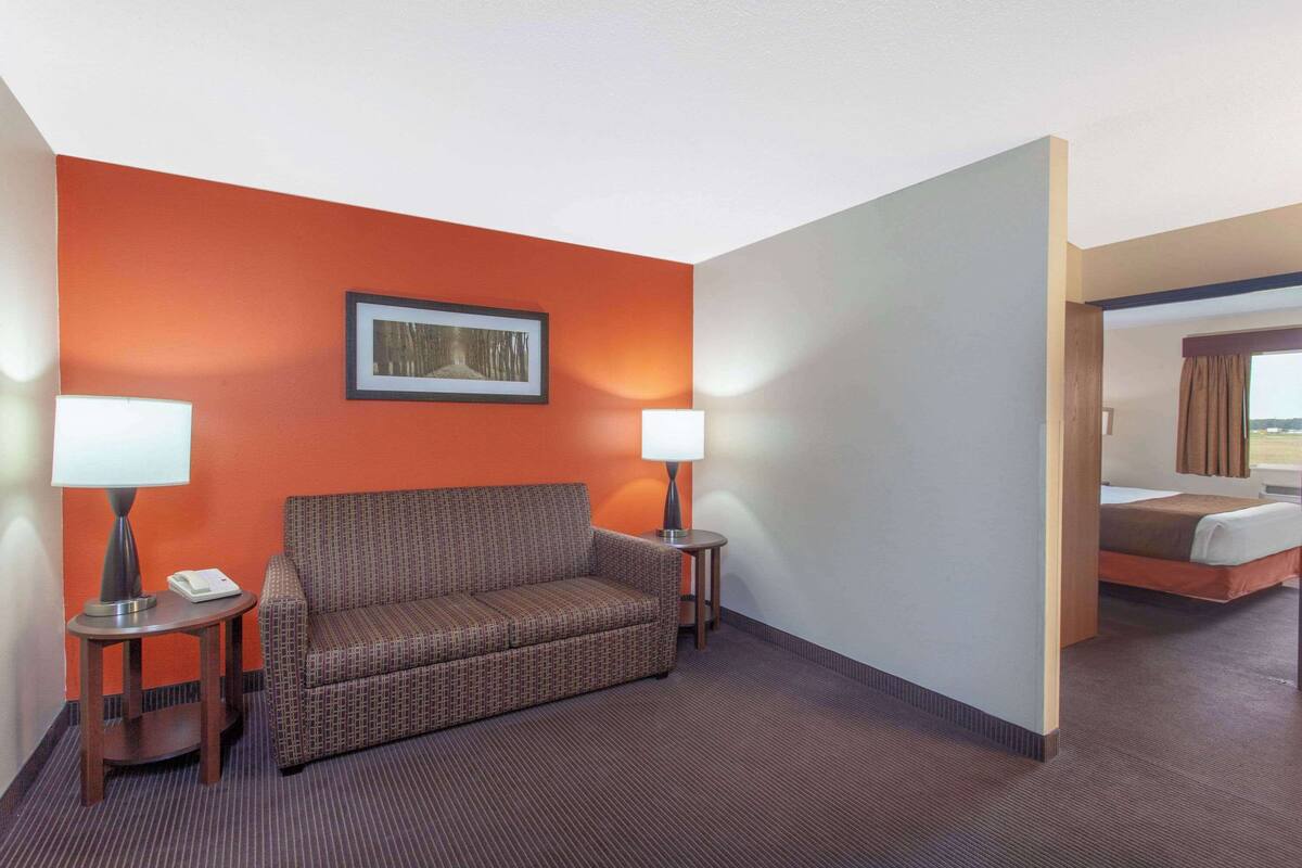 A hotel room with a patterned sofa, two bedside tables with lamps, a framed picture on the wall, and a bed with a view.