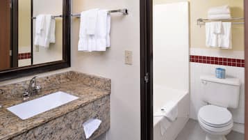 A bathroom with a granite countertop sink, a mirror, a toilet, and a bathtub.